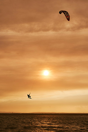 Kite surfer flies in front of the red Sun.